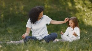 Mother and daughter bonding through yoga outdoors in a serene grassy field.