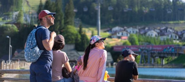 A family enjoys a sunny day sitting on a bench in Bukovel, Ukraine, with scenic mountain views.