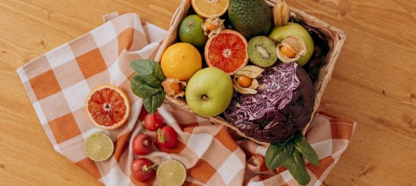 A colorful mix of fruits and vegetables arranged in a basket on a rustic wooden table.